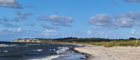Ein Strand mit Wellen, sandigem Ufer und einer Klippe im Hintergrund.