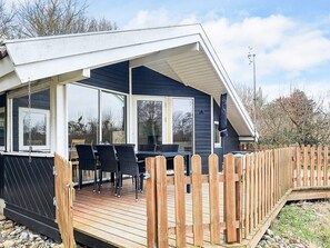 Un espacio al aire libre techado con piso de madera, sillas negras y una mesa.