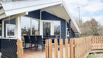 Et overdækket udendørs område med træterrasse, sorte stole og et bord.