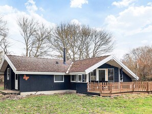Une maison à deux étages, avec un toit en tuiles, une terrasse en bois et une cour clôturée.