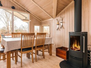 Interior de una cabaña de madera con una mesa de comedor, sillas, chimenea y ventanas amplias.