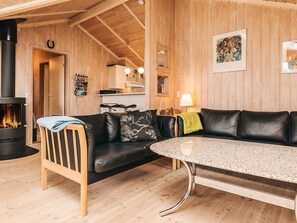 A wooden interior with a black leather sofa, a round table, and a wood-burning stove.