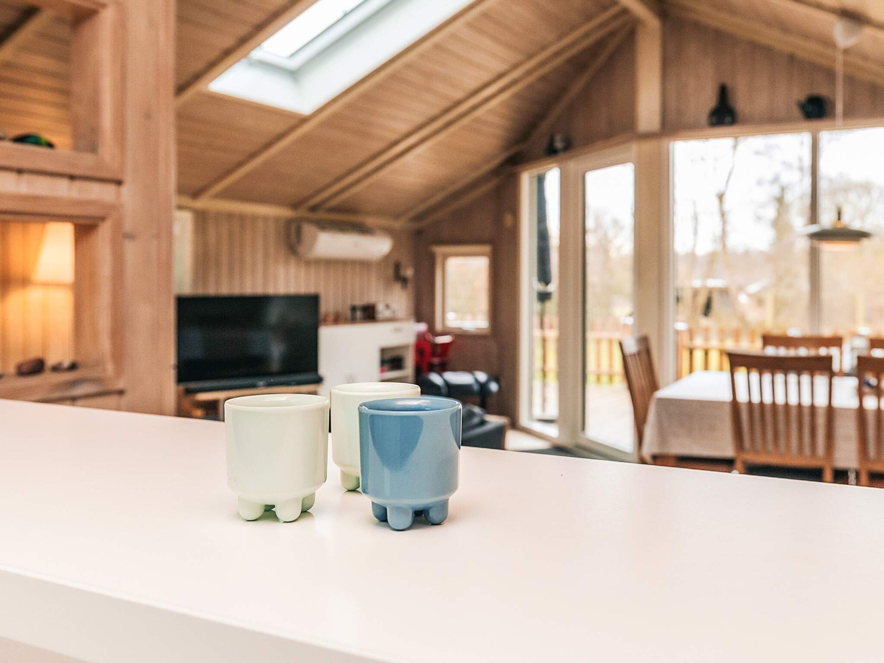 A cozy wooden interior with a dining area, a TV, and a white countertop with three mugs.