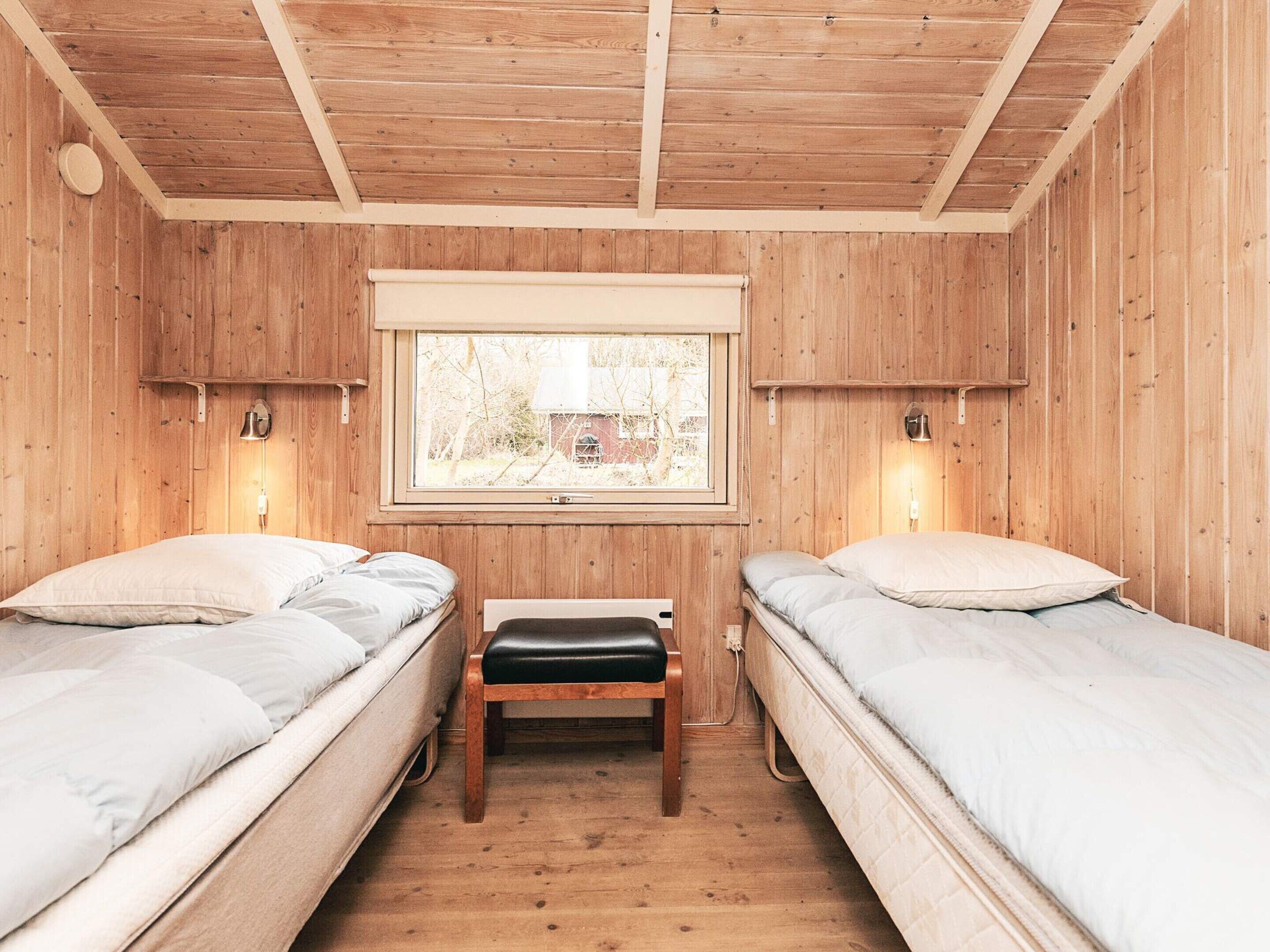 A wooden room with two beds, a bench, and a window.