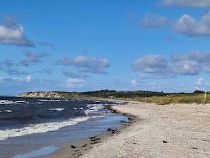 A beach with waves, a sandy shore, and a cliff in the background.