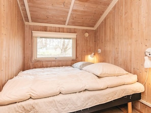A wooden room with a bed, a window, and a wall-mounted lamp.