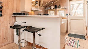 Une cuisine compacte avec des murs en bois, un plan de travail blanc, deux tabourets de bar, un lave-linge et une porte avec une fenêtre.