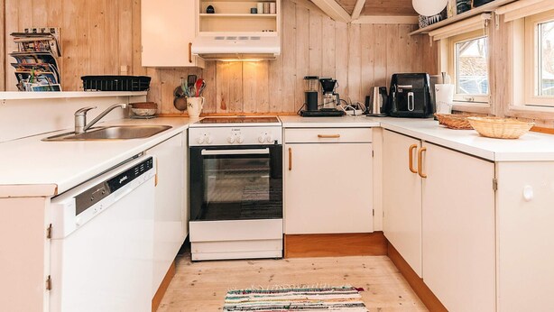 Une cuisine avec des meubles blancs, un lave-vaisselle Bosch, une cuisinière et une machine à café.