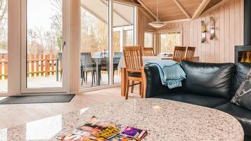 Een knus woongedeelte met een zwarte leren bank, een ronde tafel met tijdschriften, en een houten eethoek met stoelen.