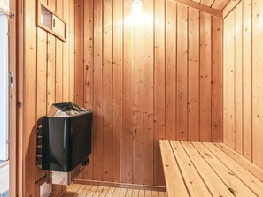 A sauna room with wooden walls, a bench, and a sauna heater.