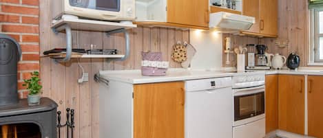Cocina compacta con estufa de leña, electrodomésticos blancos y gabinetes de madera.