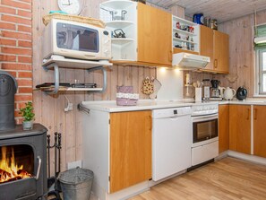 A compact kitchen with a wood stove, white appliances, and wooden cabinets.