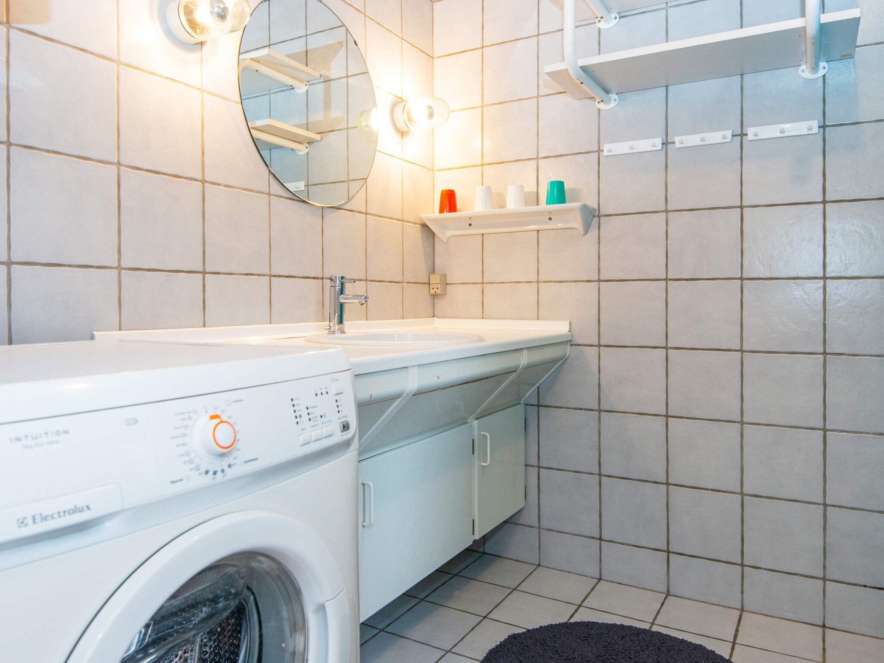 Un bagno funzionale con lavatrice, lavandino, specchio e ripiano con articoli da toilette.