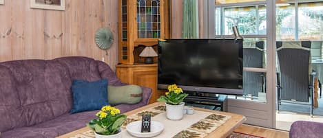 A living room with a purple sofa, a wooden cabinet, a television, and a dining area with chairs.