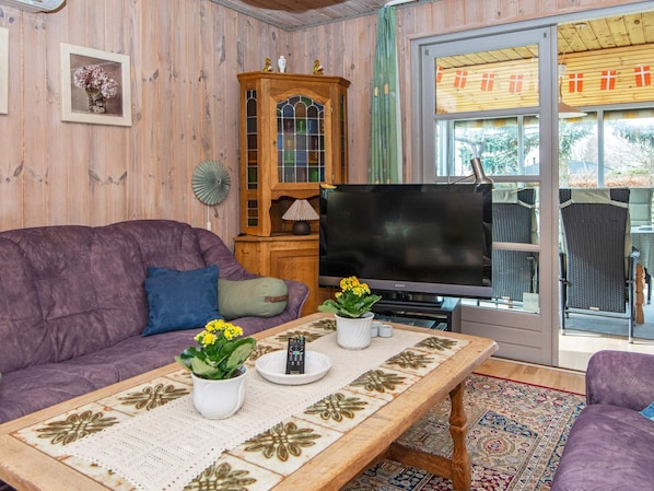 Una sala de estar con un sofá morado, un aparador de madera, un televisor y una zona de comedor con sillas.