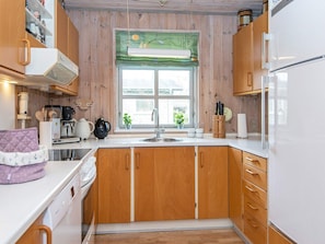 Una cocina con armarios de madera, encimera blanca, un lavamanos y una ventana con vistas al exterior.