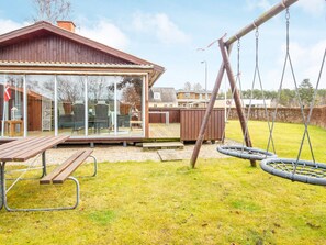 Une terrasse en bois avec une structure vitrée, une balançoire et une table de pique-nique.