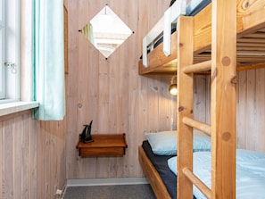 Une chambre avec un lit superposé, un mur en bois, une petite étagère et un luminaire suspendu.