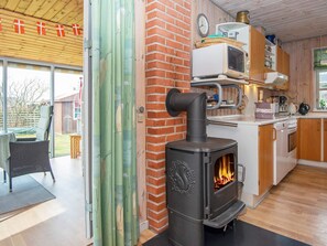 Une cuisine moderne équipée d’un poêle à bois, un coin repas avec une table et des chaises, et une vue sur l’extérieur.