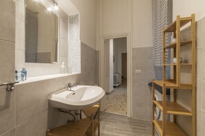 A modern bathroom with a large mirror, a white sink, and a wooden shelf unit. - Villa Albani Apartment (Rome)