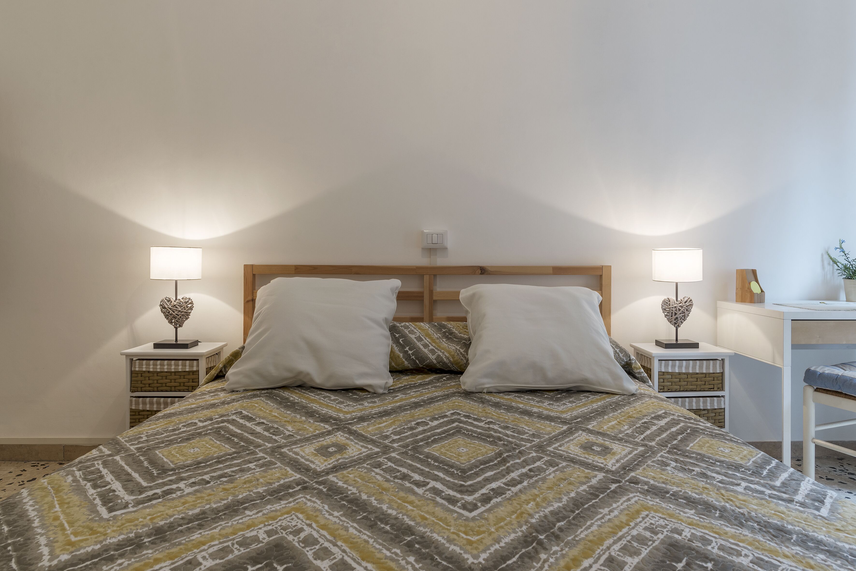 A bedroom with a bed, two bedside tables, a nightstand, a lamp, and a small table with a plant.