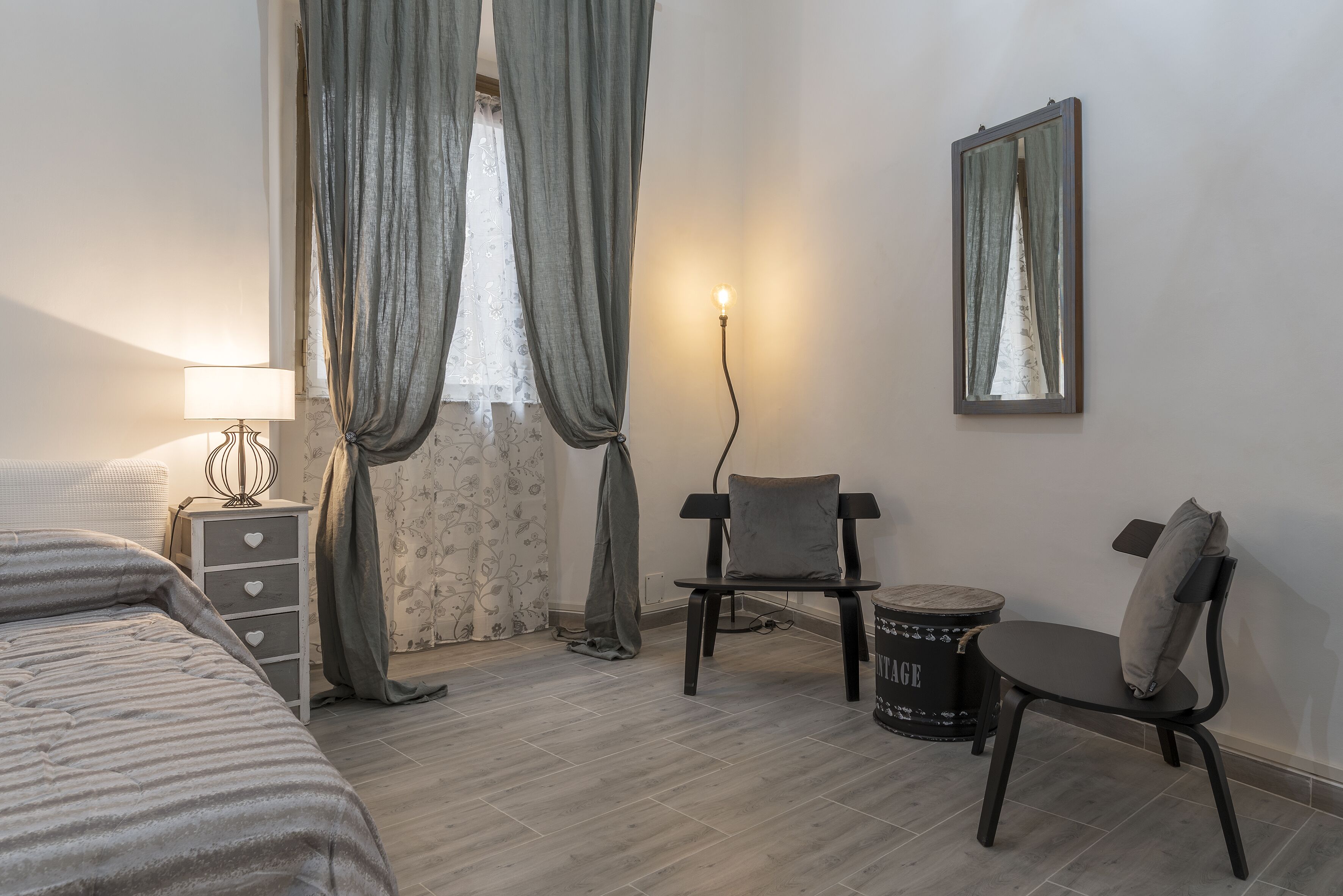 A bedroom with a bed, a bedside table with a lamp, a chair, and a small round table.