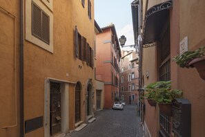 A narrow cobblestone street flanked by buildings with arched doorways and shutters, a white car parked on the right, and a street lamp. - Charming Loft Navona (Rome)