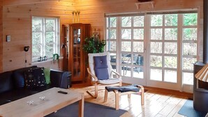 A cozy cabin interior with a wooden floor, a sofa, a dining table, and a large window with a view of trees. - Spacious Holiday Home With Sauna in Logstor (Logstor)