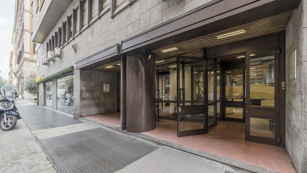 Entrada de un edificio con puerta de cristal y un pilar de metal.