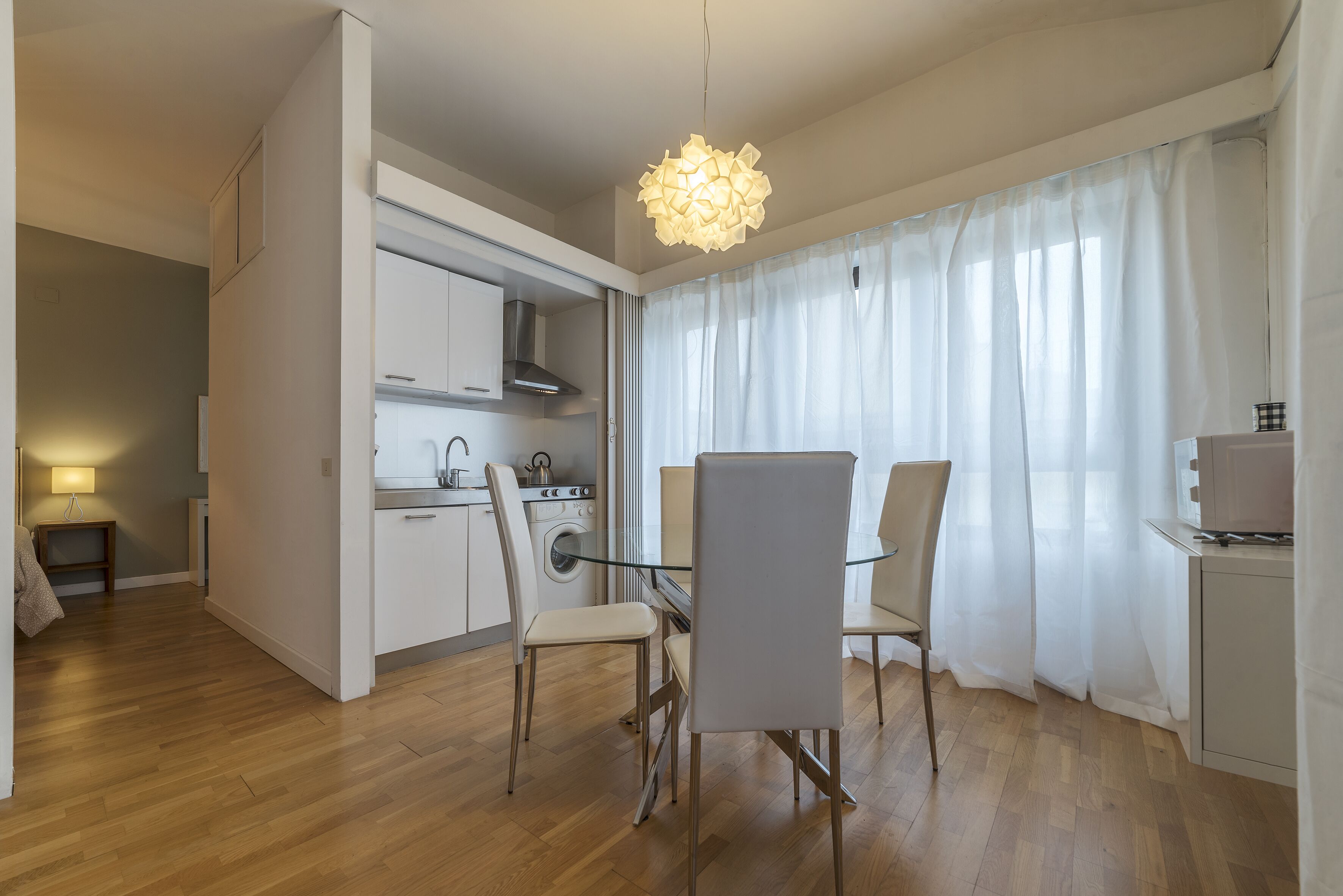 Una cocina moderna con horno integrado, lavadora y comedor con mesa y sillas de vidrio.