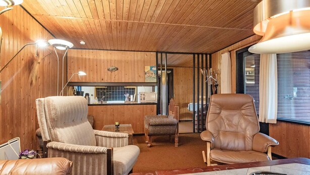 A cozy room with wooden walls, a leather sofa, a leather armchair, and a small table with a remote control.