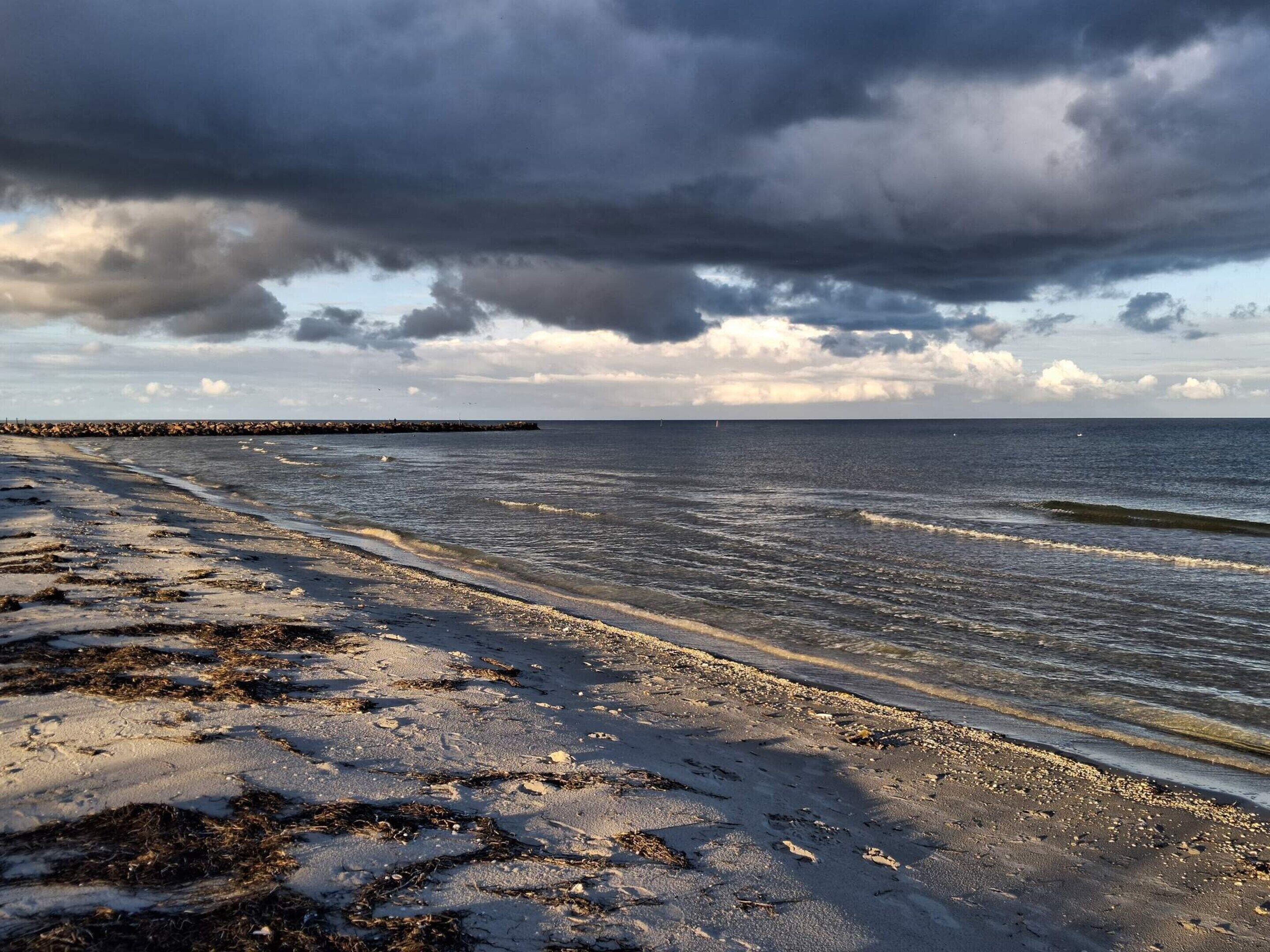 Une plage bordée d’un rivage rocheux, avec des vagues et un ciel nuageux.