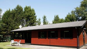 Un edificio rojo con techo plano, una antena parabólica y un arenero en el patio.