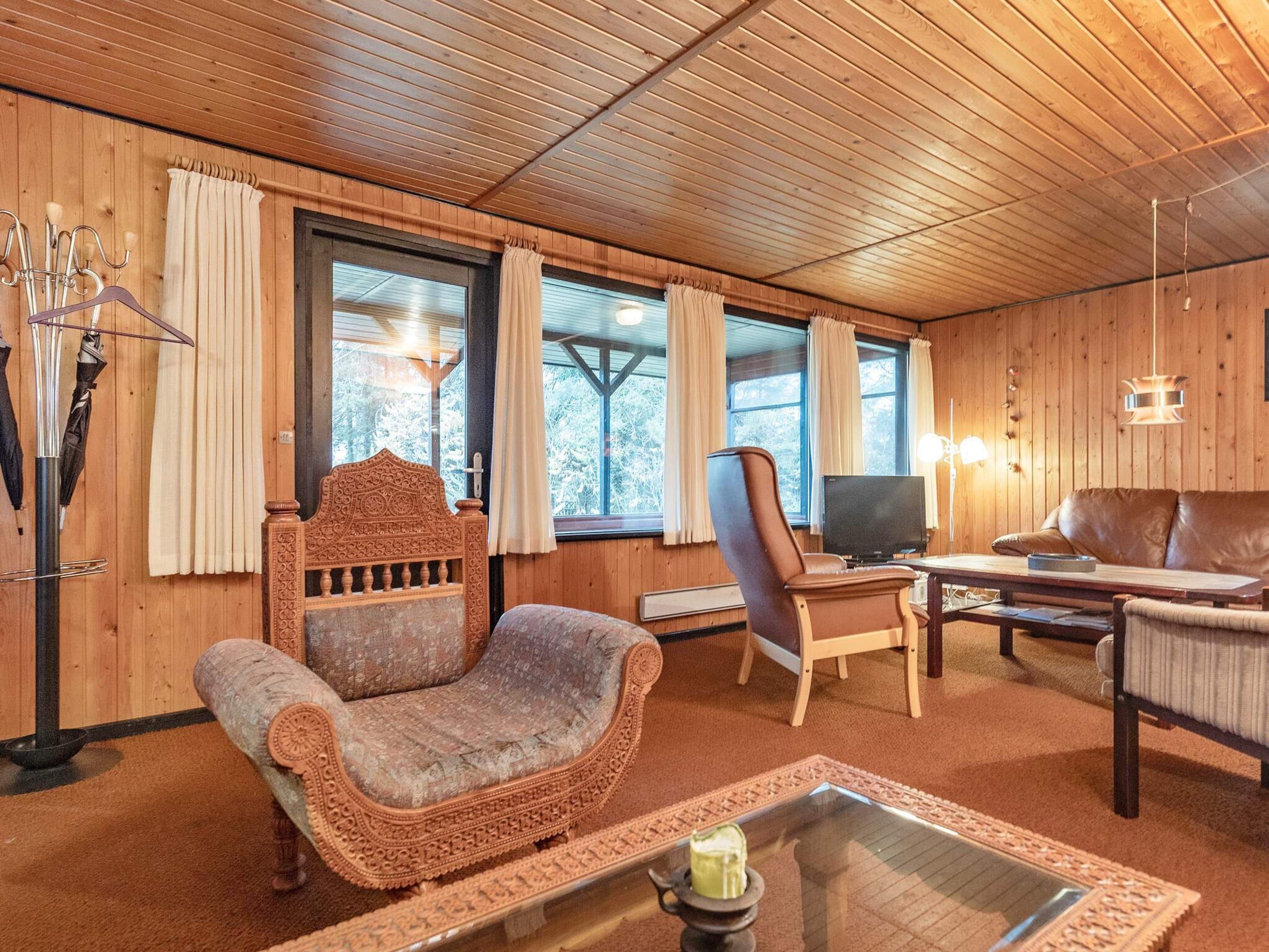 A cozy room with wooden walls, a large window, a television, and a comfortable seating area with a sofa and armchairs.