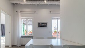 A dining area with a white table and chairs, a radiator below a window, and a framed picture on the wall. - Piazza Navona Panoramic Penthouse (Rome)