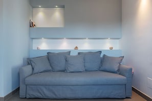 A modern living room with a grey sofa, a built-in shelf with decorative items, and recessed lighting.