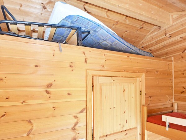 Interior de una cabaña de madera con una cama litera, una puerta y un pequeño banco.