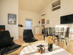 A modern living room with a dining area, featuring a flat-screen TV, a coffee table with decorative items, and a view of the adjacent bedroom. - 5 Star Holiday Home in Hals (Hals)