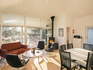 A modern living room with a fireplace, large windows, and a dining area. - 5 Star Holiday Home in Hals (Hals)