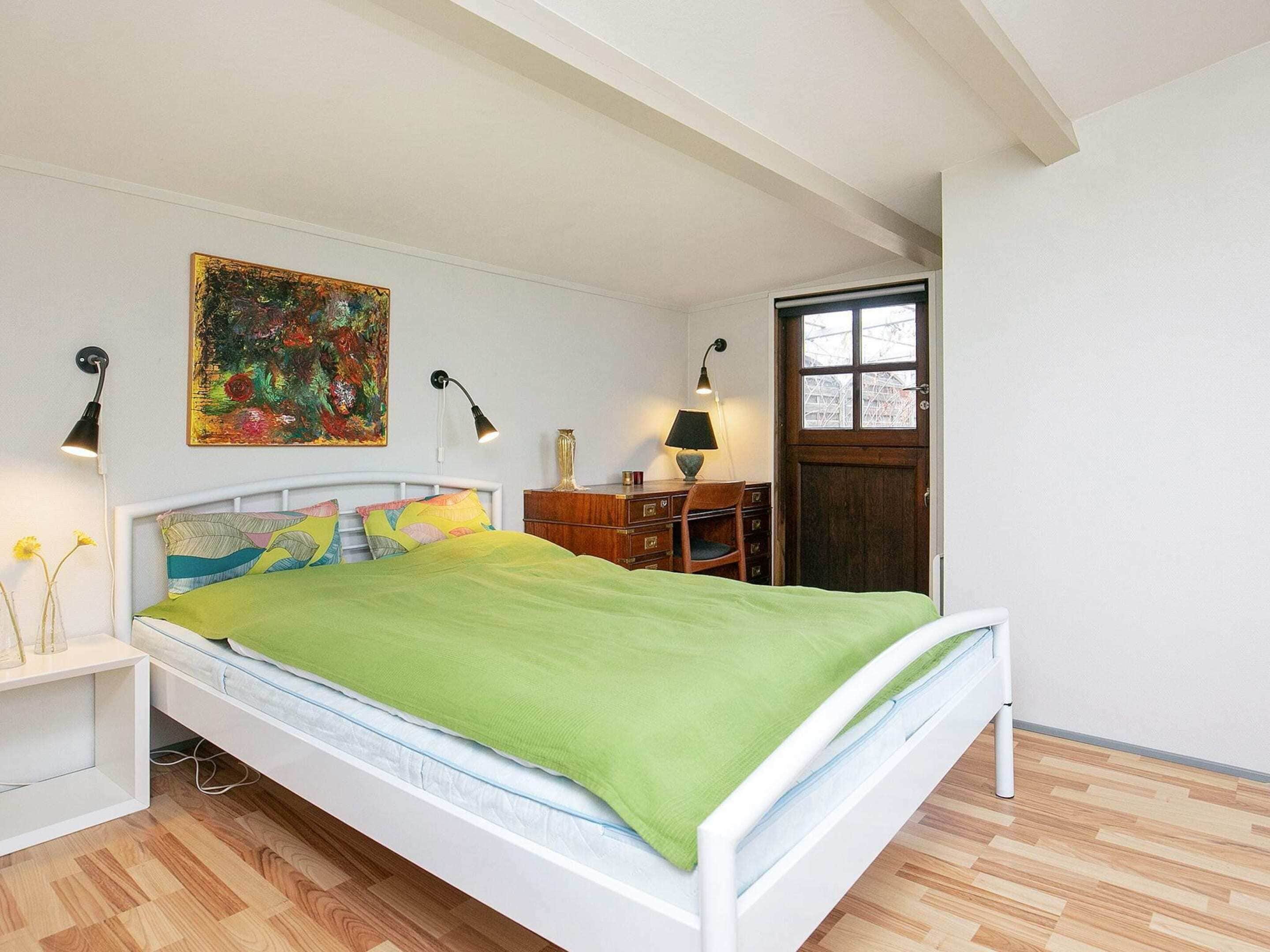 Une chambre à coucher avec un lit, des tables de chevet, un bureau, une chaise, un tableau et une fenêtre.