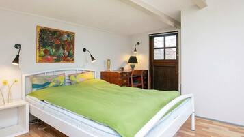 Une chambre à coucher avec un lit, des tables de chevet, un bureau, une chaise, un tableau et une fenêtre.