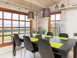 Un comedor con una mesa, sillas, plantas en macetas y ventanas amplias con vistas.