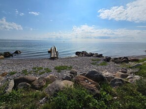 A pebbled beach with a wooden bench and large rocks. - 6 Person Holiday Home in Frorup (Frørup)