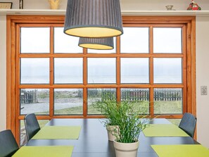 A dining area with a table and chairs, a potted plant, and a view of the sea through a large window. - 6 Person Holiday Home in Frorup (Frørup)