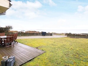 A wooden deck with a table and chairs, a grassy yard, and a view of the sea.