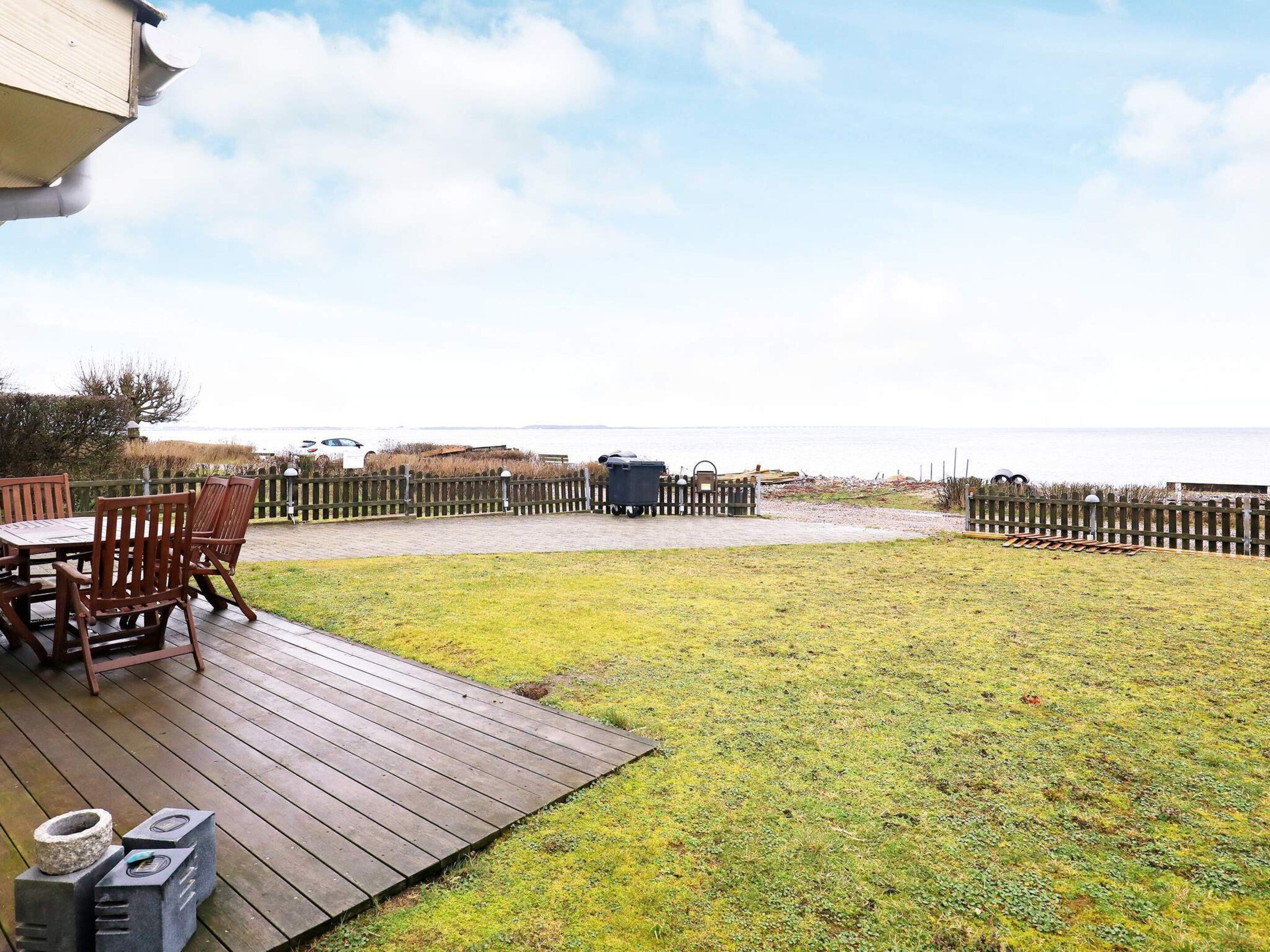 A wooden deck with a table and chairs, a grassy yard, and a view of the sea.