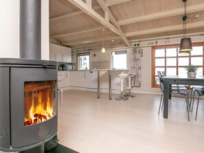 Ett modernt kök med en vedeldad spis, en matplats med bord och stolar samt ett stort fönster som släpper in naturligt ljus.