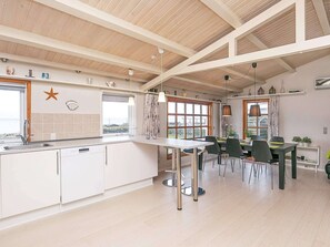 A modern kitchen with a dining area, wooden beams on the ceiling, and a view of the outdoors. - 6 Person Holiday Home in Frorup (Frørup)