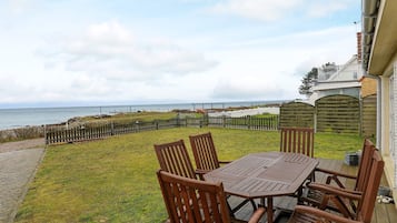 Varanda com mesa e cadeiras com vista para uma área gramada e o mar.