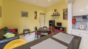 A living room with a sofa, a dining table, and chairs. There is a kitchen area with a microwave and a kettle. - Pigneto Colourful Apartment (Rome)